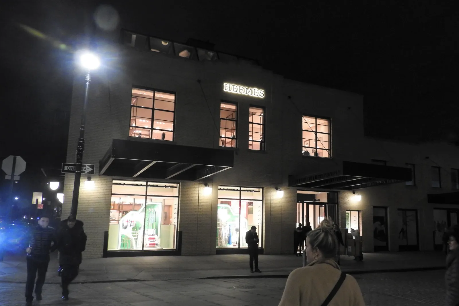 Illuminated Hermès storefront on Gansevoort Street at night, with pedestrians crossing in front.